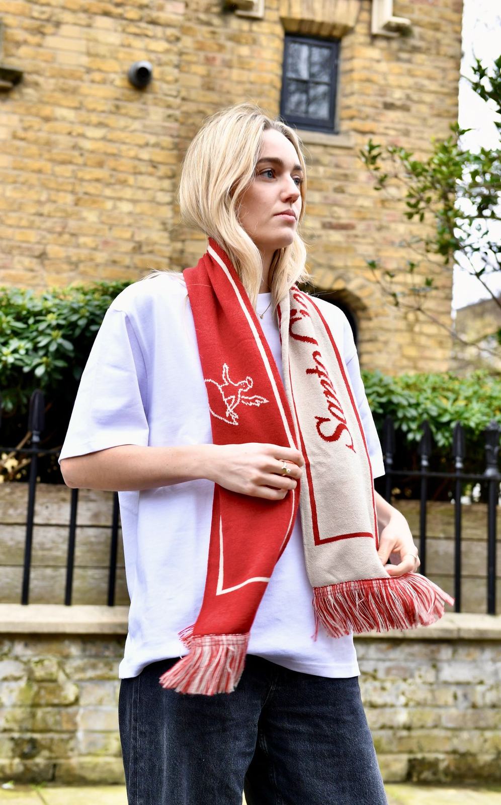 The red and cream Santo Cielo OG scarf with the angel and script, worn over a white tee on a London street
