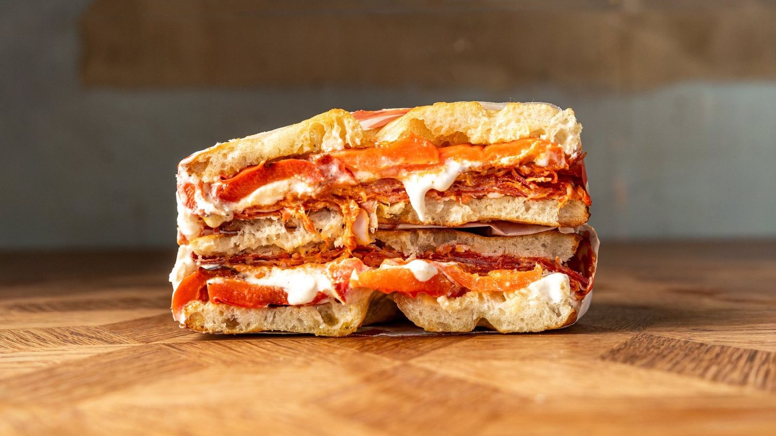 The Vesuvius schiacciata cut in half showing spicy salami, stracciatella, 'nduja crema and roasted red peppers on Tuscan bread
